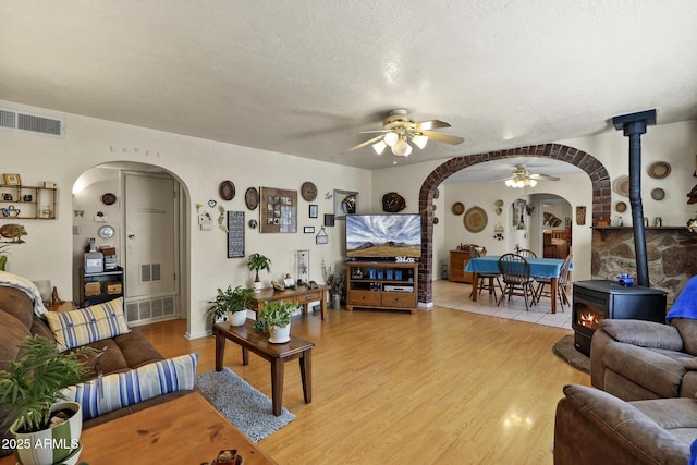 living room with hardwood / wood-style flooring, a wood stove, a textured ceiling, and ceiling fan