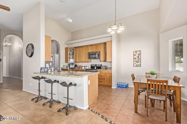 kitchen with arched walkways, a breakfast bar area, light tile patterned flooring, appliances with stainless steel finishes, and glass insert cabinets