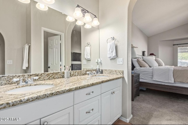 ensuite bathroom featuring a sink, double vanity, connected bathroom, and lofted ceiling