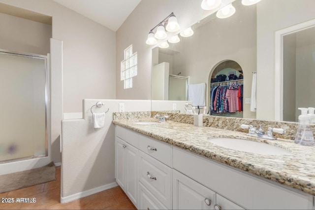 full bath featuring a stall shower, double vanity, a sink, and tile patterned floors