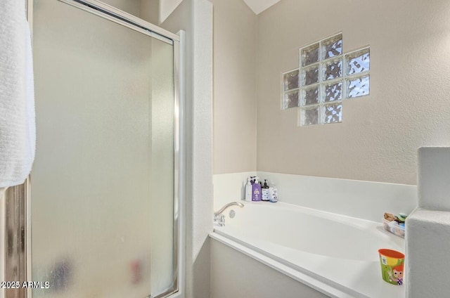 bathroom with a textured wall, a shower stall, and a bath