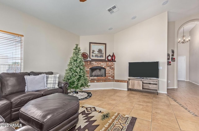 tiled living room with arched walkways, visible vents, an inviting chandelier, a brick fireplace, and baseboards