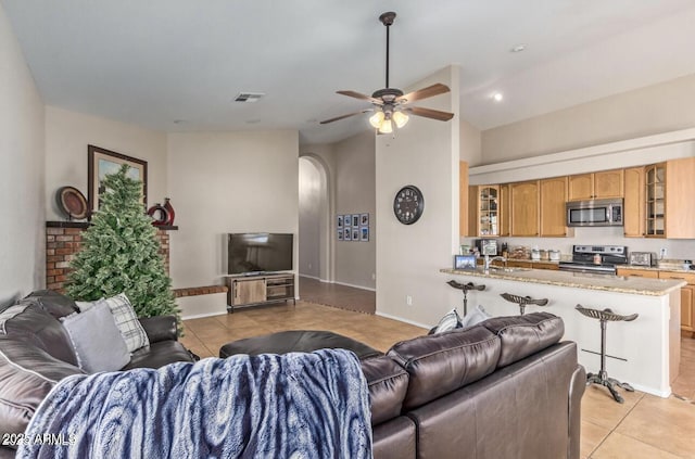 living area with light tile patterned floors, visible vents, arched walkways, baseboards, and a ceiling fan