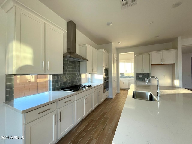 kitchen featuring stainless steel appliances, white cabinetry, sink, and wall chimney exhaust hood