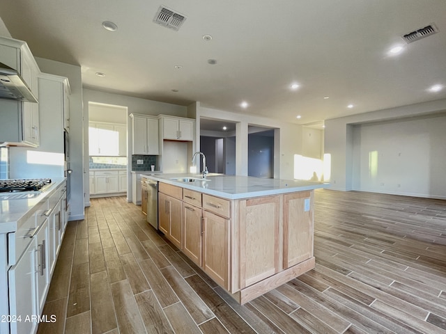 kitchen featuring sink, wall chimney range hood, appliances with stainless steel finishes, a large island with sink, and light brown cabinets