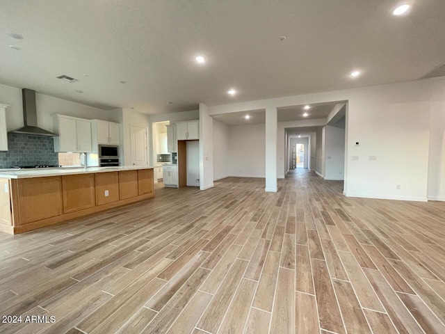 kitchen with a large island, white cabinets, light hardwood / wood-style floors, and wall chimney exhaust hood