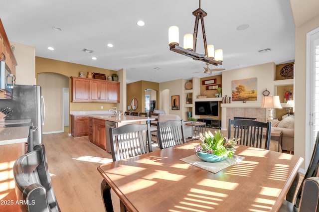 dining area with light hardwood / wood-style floors, sink, a notable chandelier, and a tiled fireplace