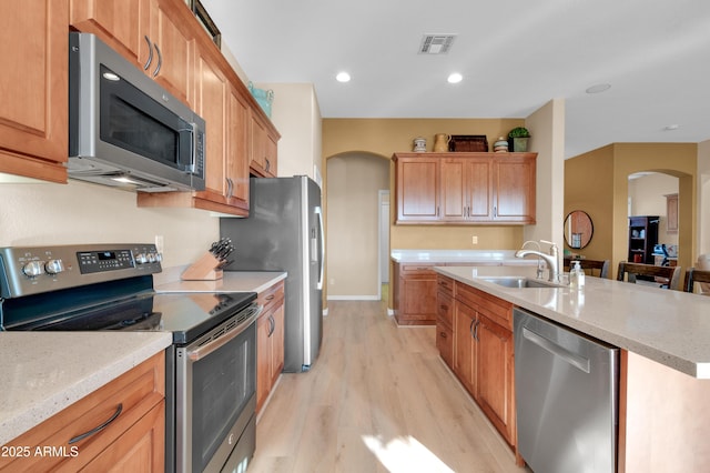 kitchen featuring sink, a center island with sink, stainless steel appliances, and light wood-type flooring