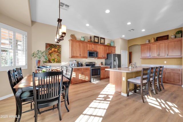 kitchen featuring decorative light fixtures, sink, light hardwood / wood-style flooring, an island with sink, and stainless steel appliances