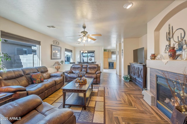 living room featuring a tiled fireplace, ceiling fan, and parquet flooring