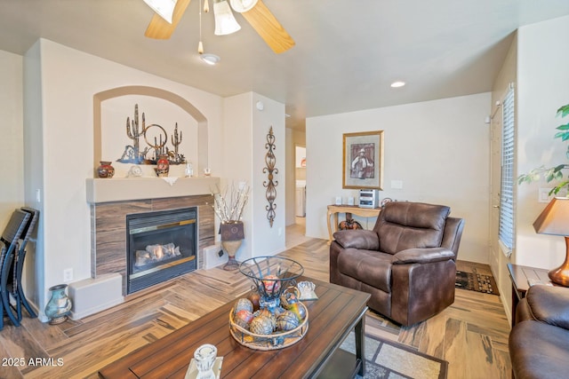 living room featuring light parquet floors, ceiling fan, and a tiled fireplace