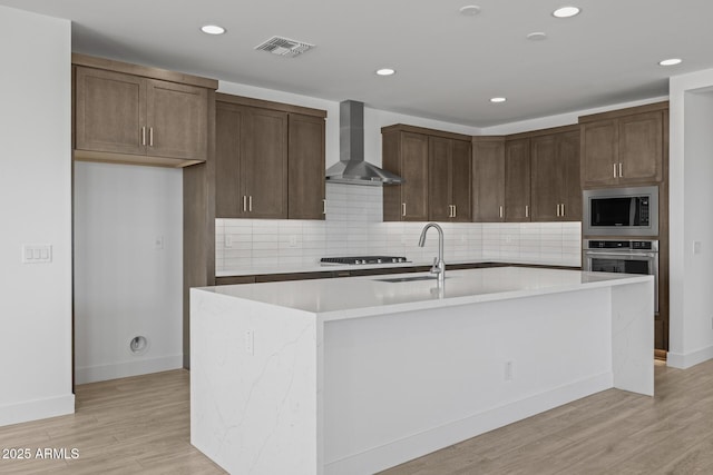 kitchen featuring visible vents, a sink, light countertops, stainless steel appliances, and wall chimney exhaust hood