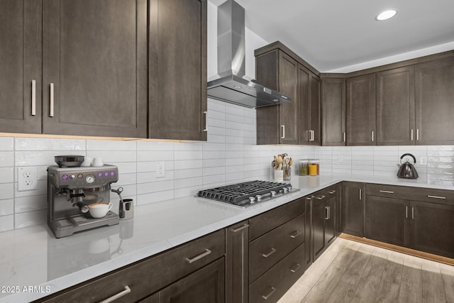 kitchen with decorative backsplash, dark brown cabinetry, wall chimney range hood, and stainless steel gas stovetop