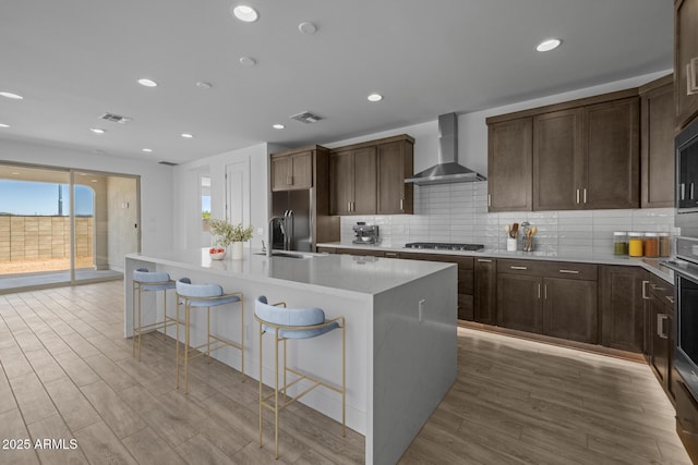 kitchen featuring wall chimney range hood, visible vents, a sink, and light wood-style flooring