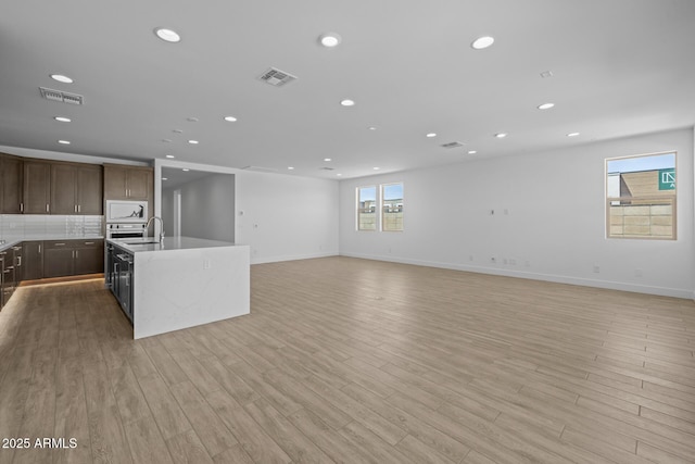 kitchen with light countertops, a kitchen island with sink, white microwave, and visible vents