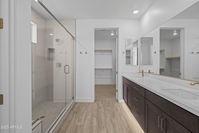 bathroom with a spacious closet, a shower stall, a sink, and wood finished floors