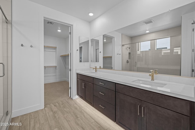 full bath with a sink, a walk in closet, wood finished floors, and a shower stall