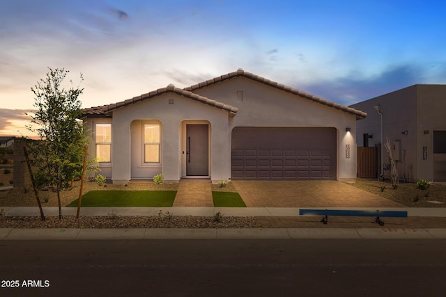view of front of house with decorative driveway, a garage, stucco siding, and a tiled roof