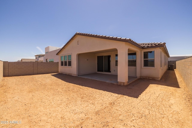 rear view of property featuring a fenced backyard, a patio, stucco siding, and a tiled roof