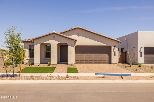 view of front of house featuring stucco siding, driveway, a tile roof, and a garage