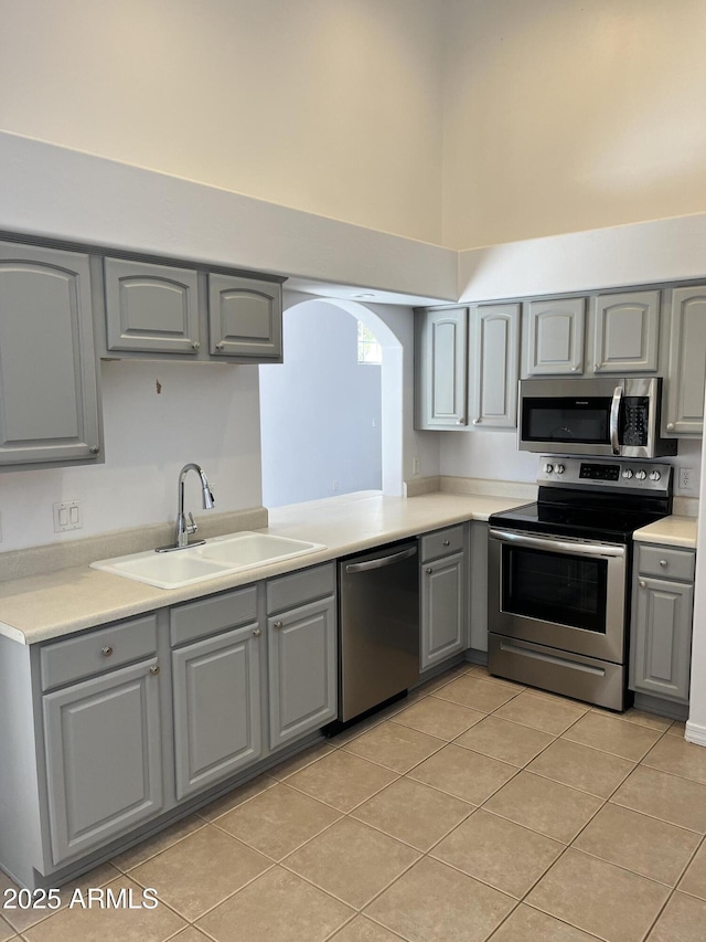 kitchen featuring gray cabinetry, sink, light tile patterned floors, and stainless steel appliances