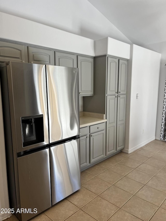 kitchen with gray cabinetry, lofted ceiling, stainless steel fridge with ice dispenser, and light tile patterned floors