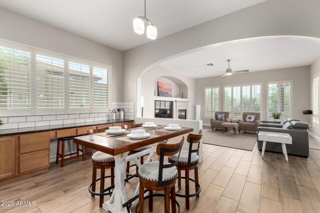 16201 S 29th Ave, Phoenix, AZ 85045 - dining room featuring a ceiling fan, visible vents, arched walkways, a glass covered fireplace, and light wood-style floors