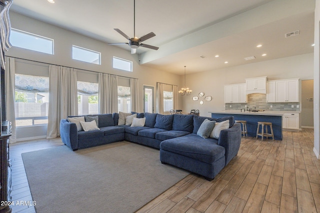 living room featuring light hardwood / wood-style floors, ceiling fan with notable chandelier, and a high ceiling