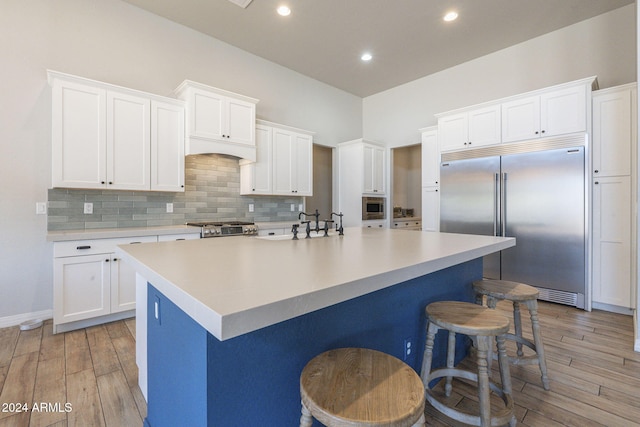 kitchen with built in appliances, white cabinetry, and a kitchen island with sink