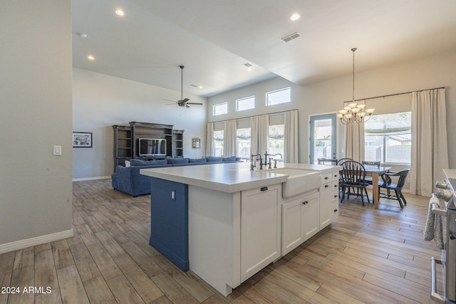 kitchen with a center island with sink, light wood-type flooring, sink, white cabinets, and ceiling fan with notable chandelier