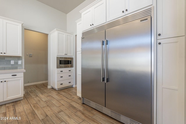 kitchen featuring white cabinetry, light wood-type flooring, decorative backsplash, and built in appliances