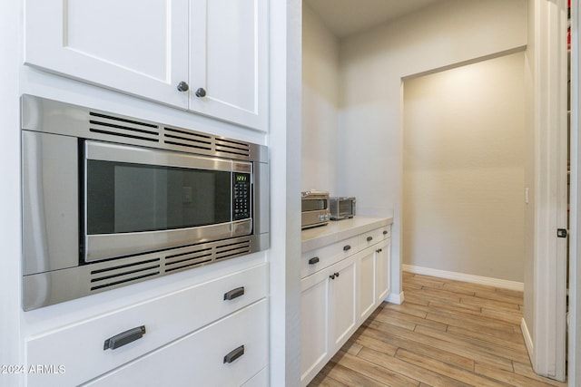 kitchen featuring stainless steel microwave, light hardwood / wood-style floors, and white cabinets