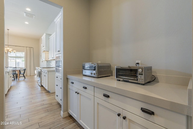 kitchen with light hardwood / wood-style flooring, white cabinetry, decorative light fixtures, and stainless steel appliances