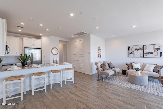 kitchen featuring a breakfast bar, white cabinets, stainless steel fridge, light wood-type flooring, and light stone counters