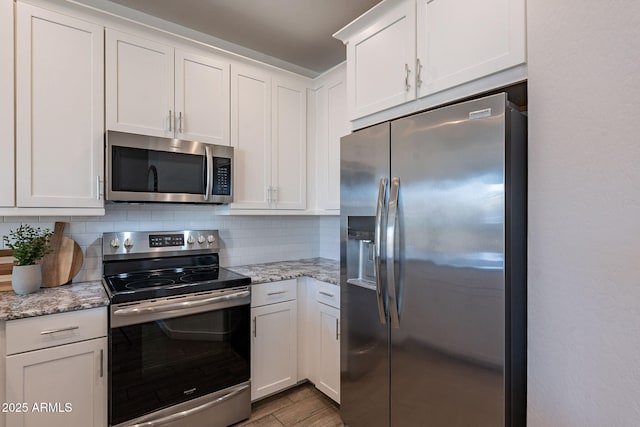 kitchen with white cabinets, appliances with stainless steel finishes, backsplash, and light stone counters