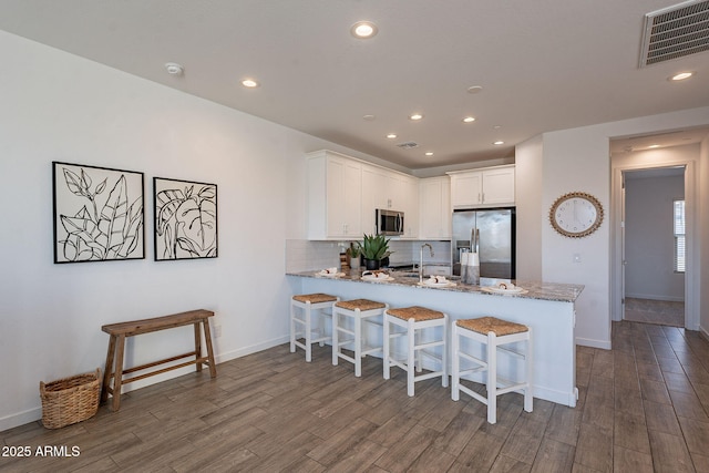 kitchen with white cabinets, kitchen peninsula, stainless steel appliances, and hardwood / wood-style flooring