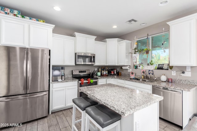 kitchen featuring white cabinetry, sink, a center island, stainless steel appliances, and light stone counters