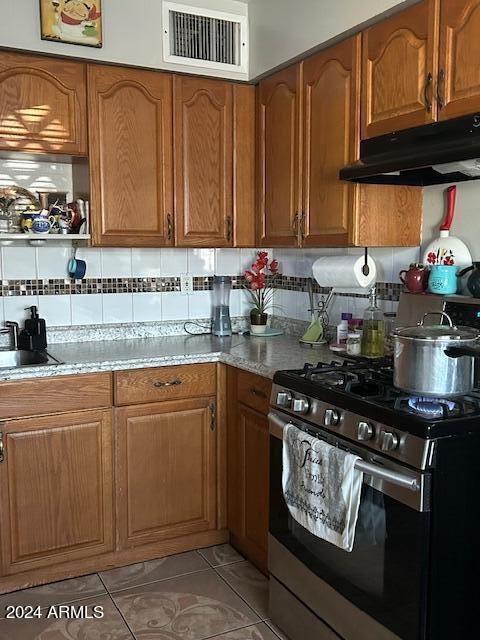 kitchen with stainless steel range with gas cooktop, tasteful backsplash, sink, light stone counters, and light tile patterned flooring