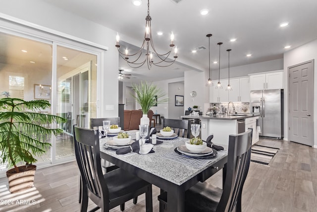 dining area featuring ceiling fan with notable chandelier, sink, and light wood-type flooring