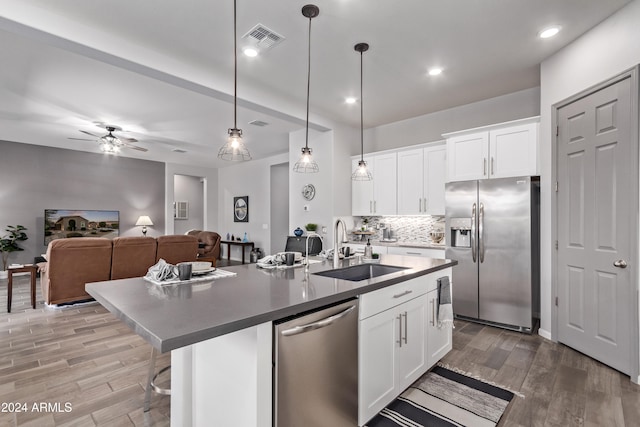 kitchen with stainless steel appliances, sink, an island with sink, white cabinets, and pendant lighting