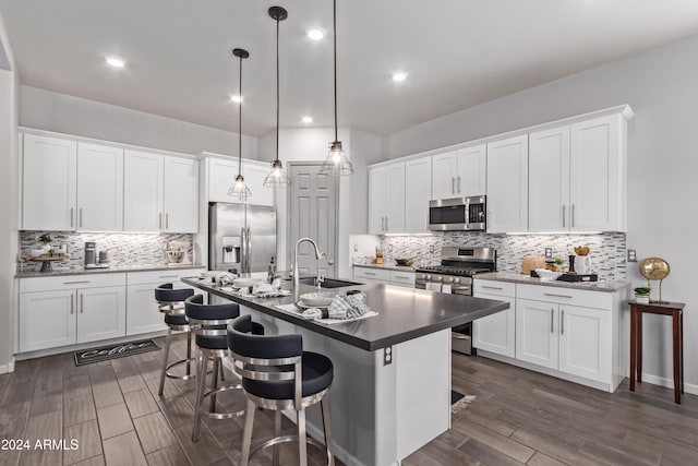 kitchen with a kitchen bar, stainless steel appliances, white cabinets, sink, and decorative light fixtures