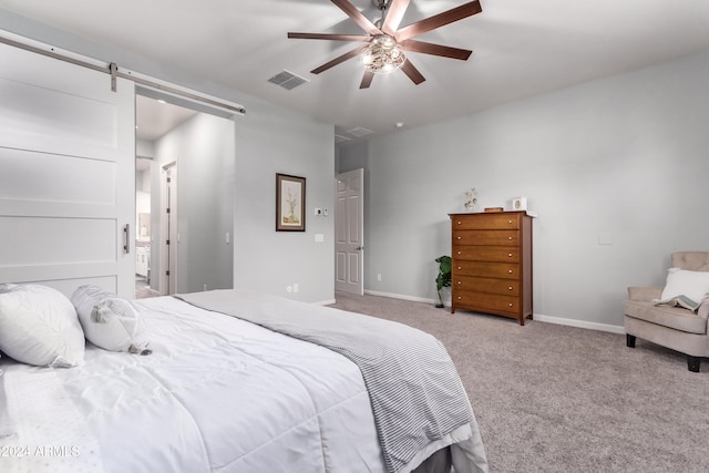 carpeted bedroom with a barn door and ceiling fan