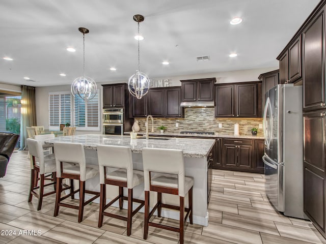 kitchen with an island with sink, decorative light fixtures, light hardwood / wood-style floors, a kitchen bar, and stainless steel appliances