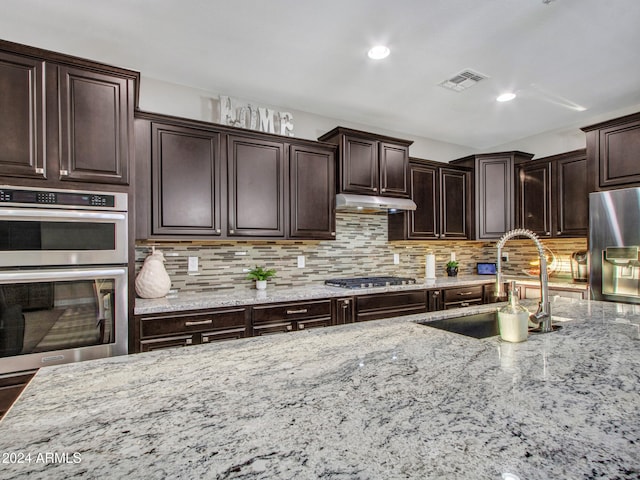 kitchen featuring sink, light stone counters, backsplash, dark brown cabinets, and appliances with stainless steel finishes