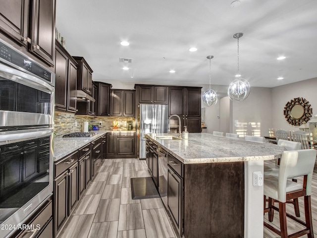 kitchen with sink, an island with sink, pendant lighting, a breakfast bar, and appliances with stainless steel finishes