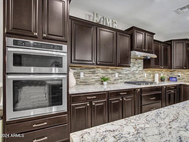 kitchen featuring appliances with stainless steel finishes, backsplash, light stone counters, and dark brown cabinets