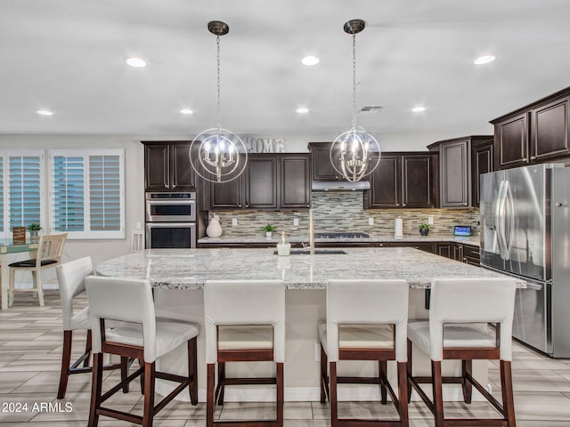 kitchen with a kitchen bar, a kitchen island with sink, pendant lighting, and appliances with stainless steel finishes