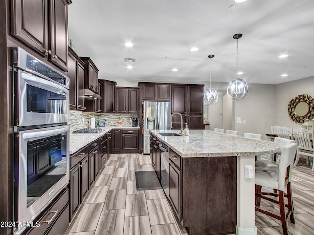 kitchen featuring appliances with stainless steel finishes, a kitchen breakfast bar, a kitchen island with sink, sink, and decorative light fixtures