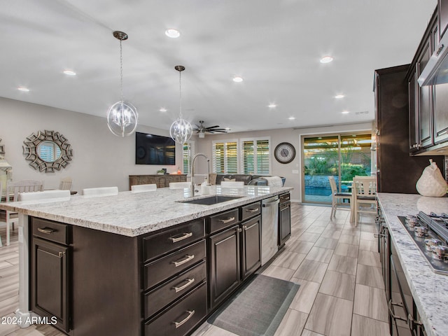 kitchen with dark brown cabinetry, ceiling fan, sink, decorative light fixtures, and a center island with sink