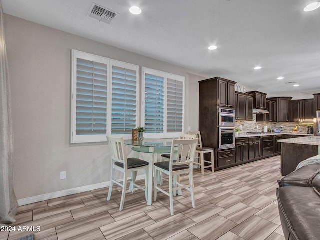 kitchen with tasteful backsplash, light stone counters, dark brown cabinets, and appliances with stainless steel finishes